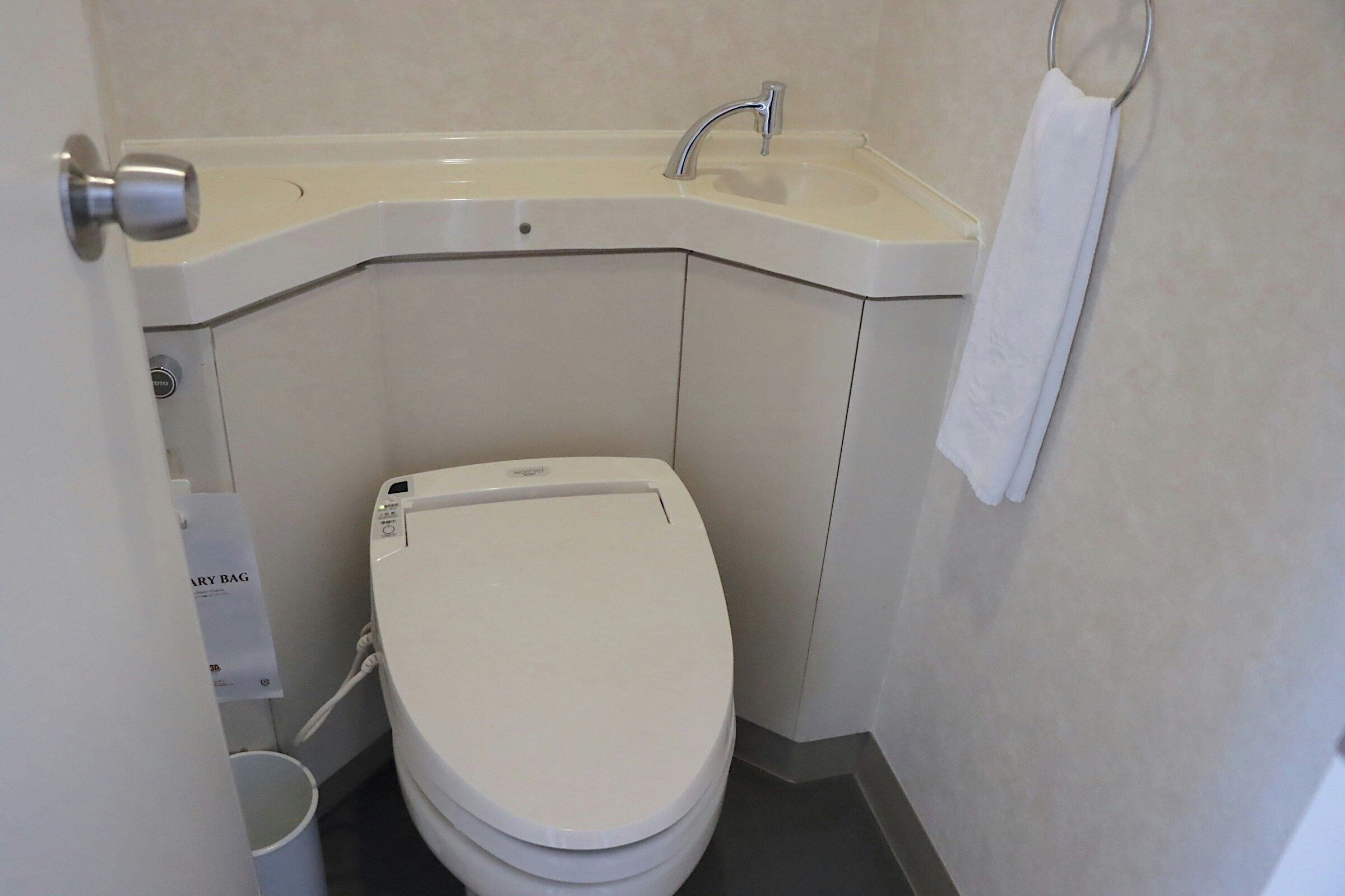 A bathroom with a white toilet, a sink with a faucet, and a towel hanging on a metal ring.