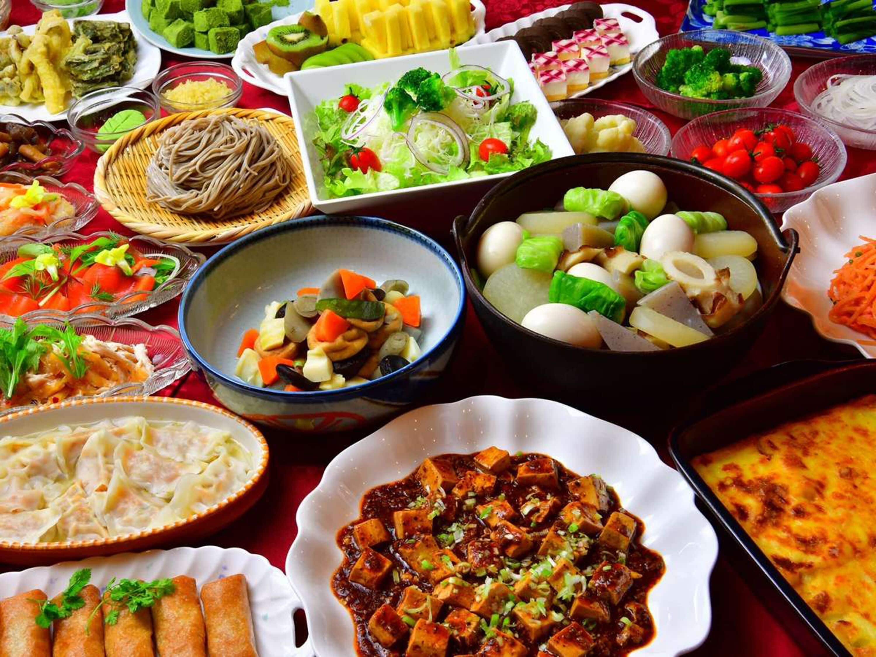 A variety of dishes on a table, including a bowl of tofu, a plate of noodles, and several side dishes.