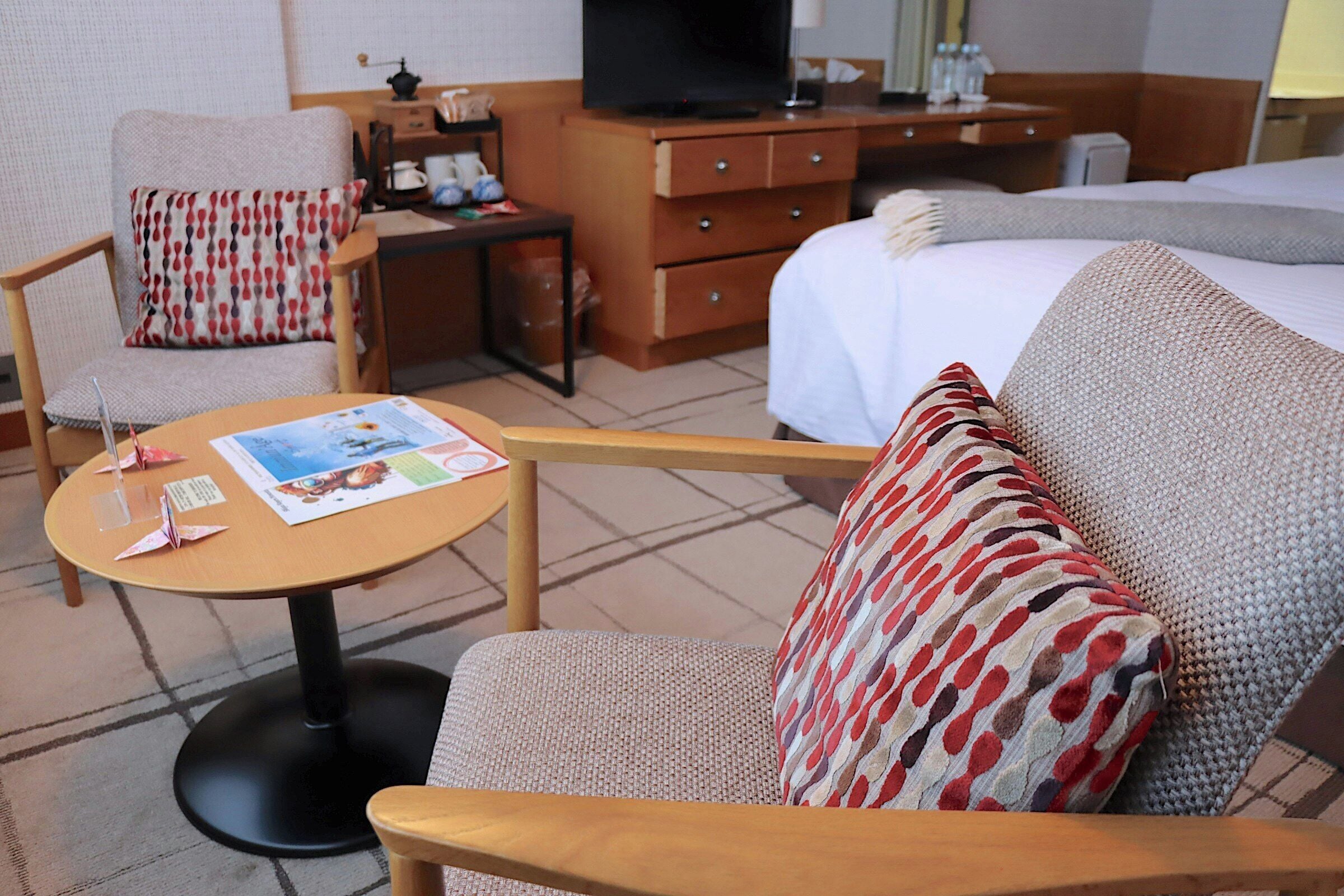 A hotel room with a bed, a desk, a chair, a table, and a television.
