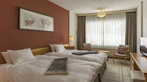 A hotel room with two beds, a desk, a chair, a television, and a window with curtains.