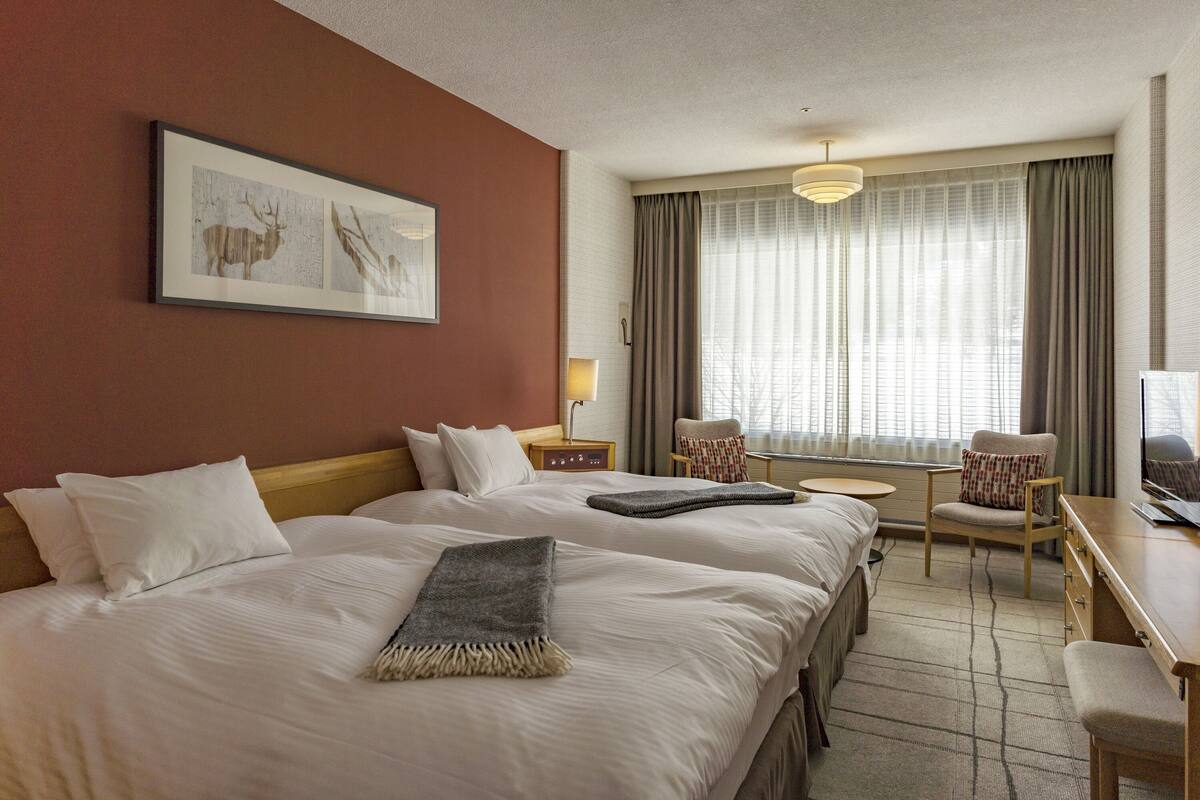 Habitación de hotel con dos camas, un escritorio, una silla, un televisor y una ventana con cortinas.