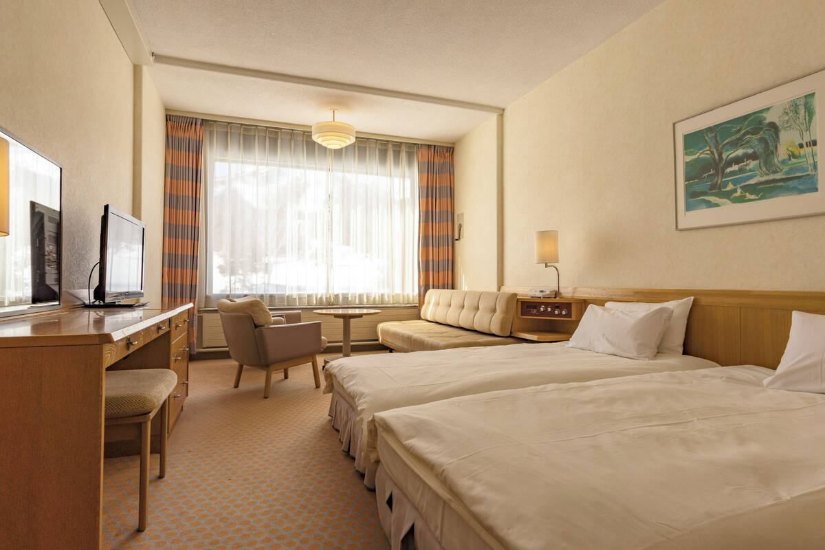 Habitación de hotel con dos camas, un escritorio, una silla, una mesita y un cuadro en la pared.