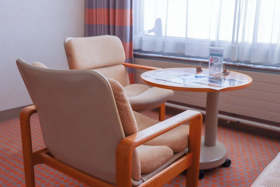A hotel room with a single chair and a small round table with a magazine.