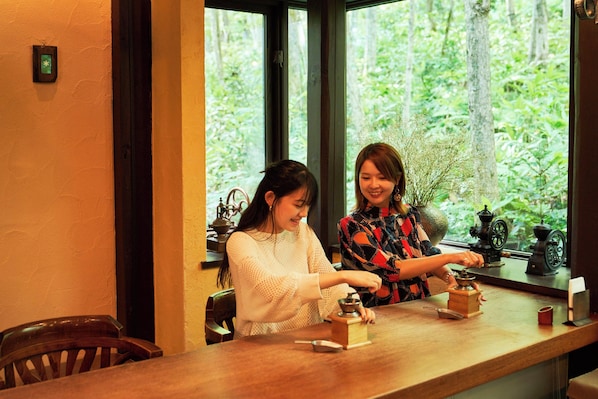 Two individuals at a wooden table with a window view of greenery. - Shin Furano Prince Hotel (Furano)