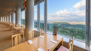Un salón de conferencias con una larga mesa y sillas, amplias ventanas que ofrecen vistas a un paisaje urbano y colinas.