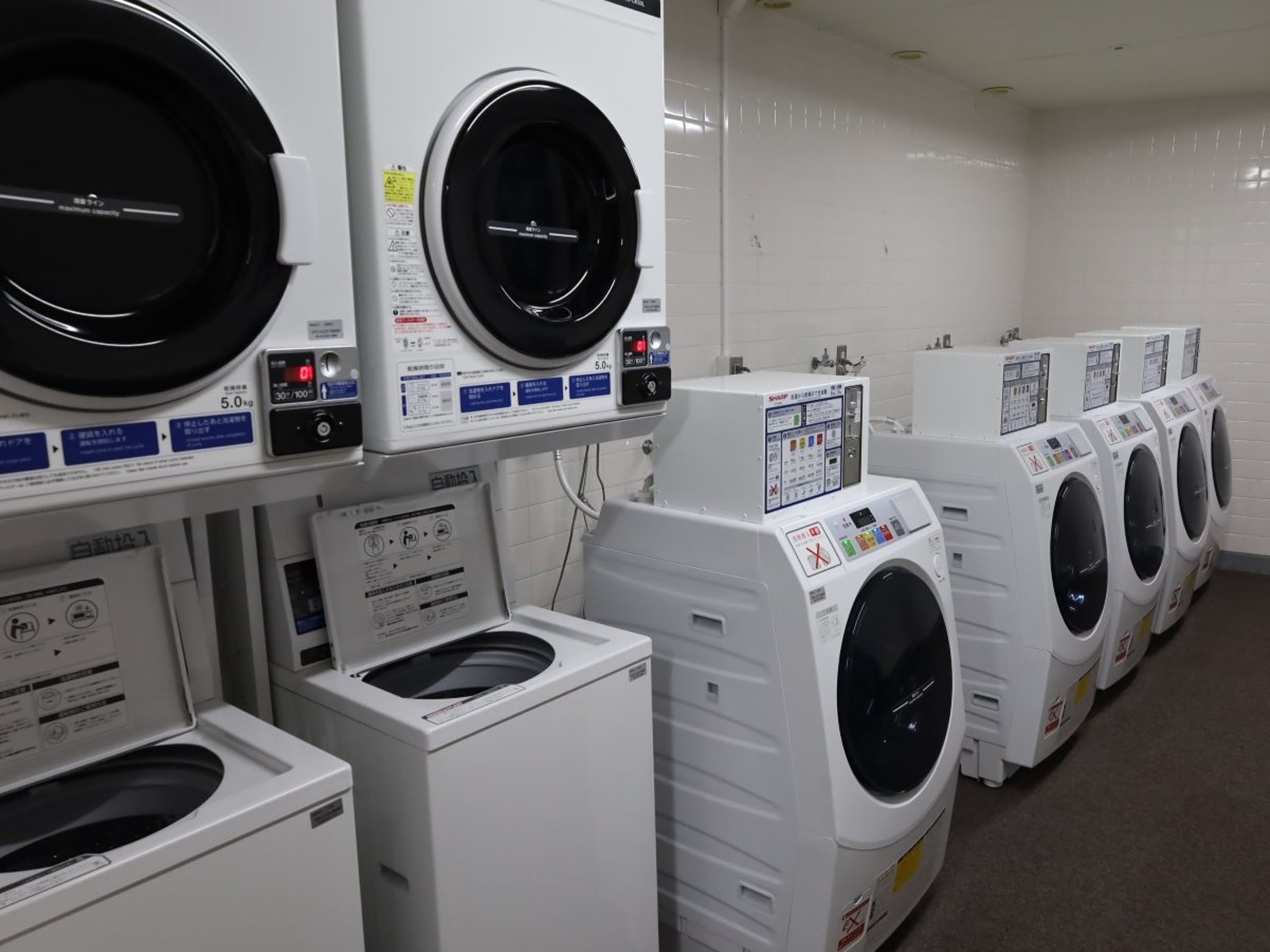 A row of white front-loading washing machines in a commercial laundry room.