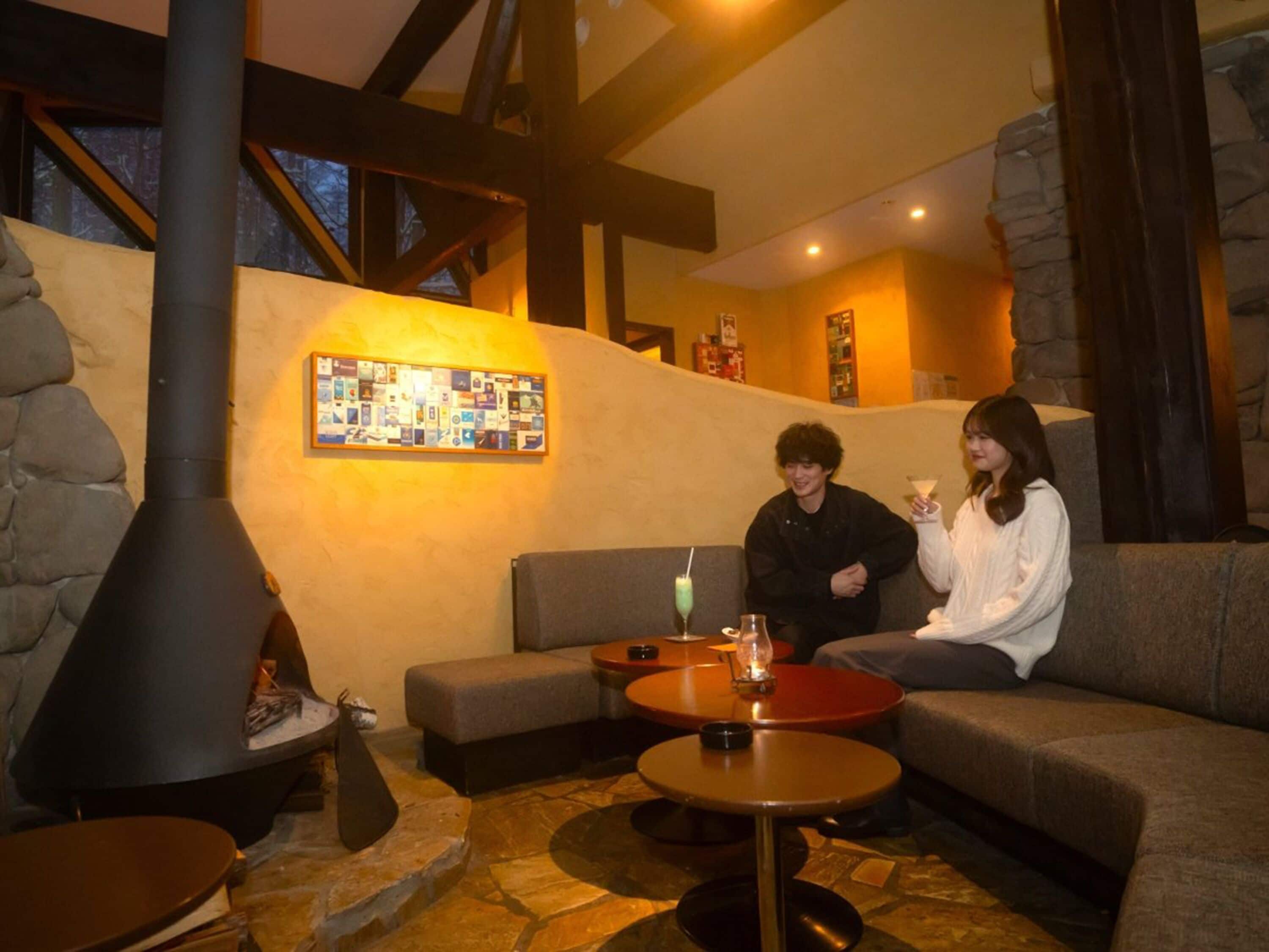 Un interior acogedor con paredes de piedra, una chimenea grande y una zona de estar con mesas y cojines.