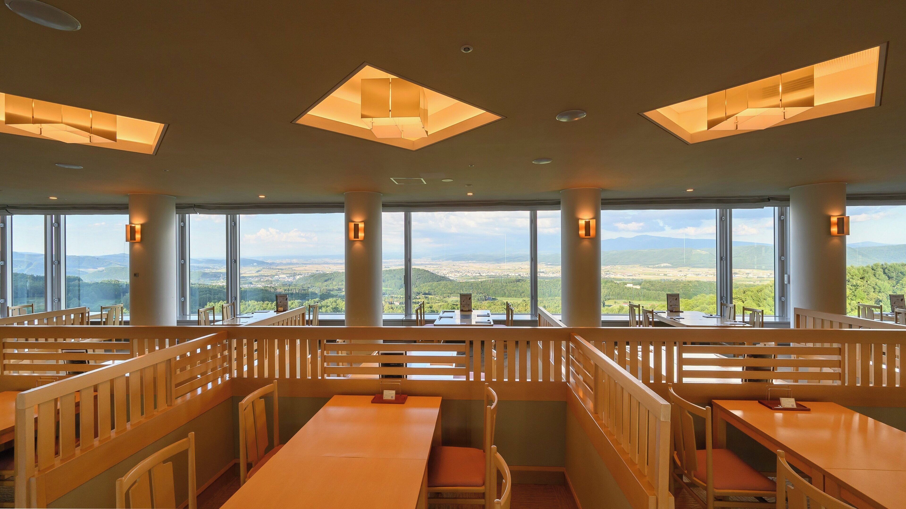 Un restaurant avec des tables hautes et des bancs, de grandes fenêtres donnant sur le paysage et des luminaires suspendus.