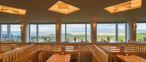 A restaurant with high tables and benches, large windows offering a view of the landscape, and pendant lighting.