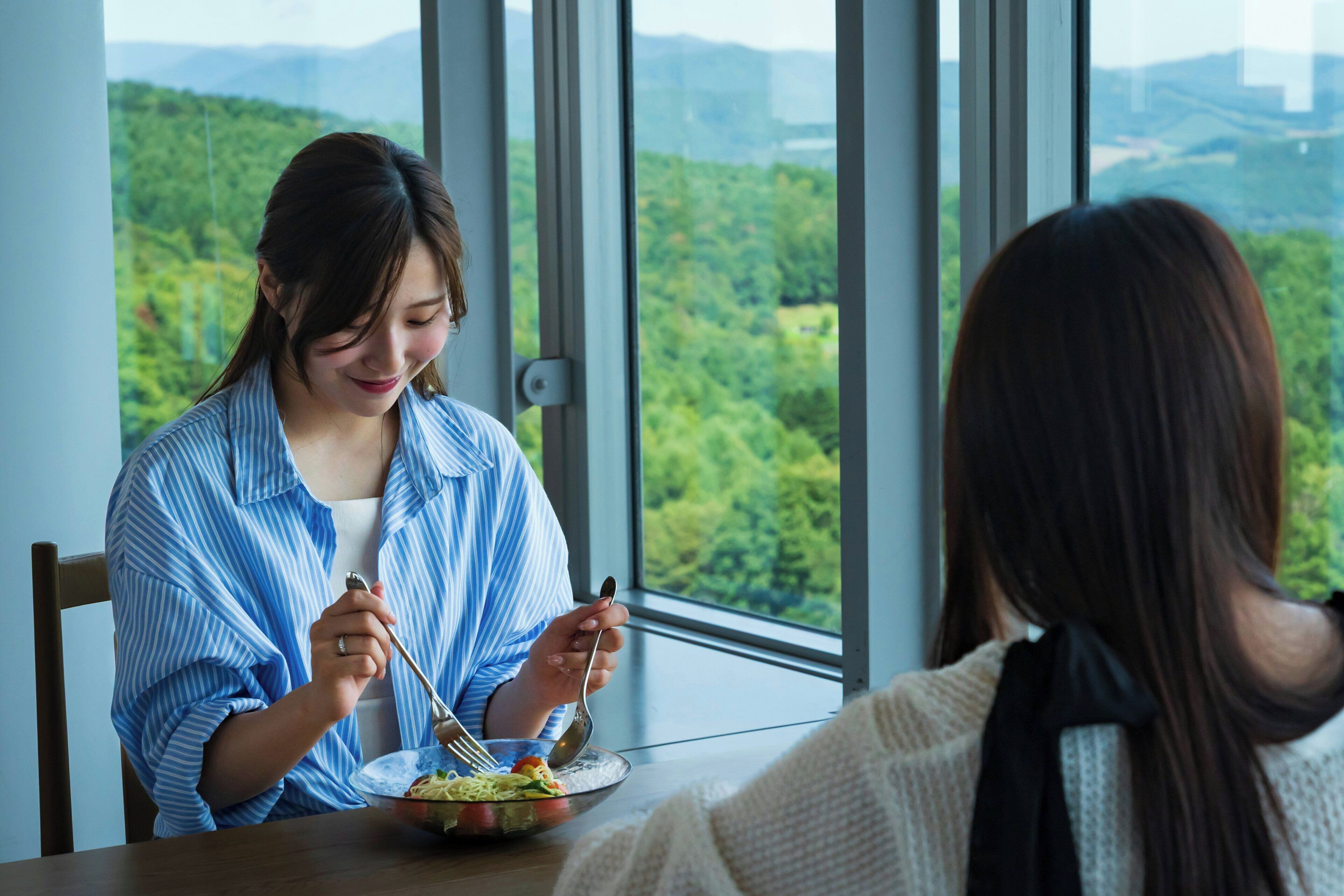 Two people dining at a table with a view of a forested landscape through large windows.