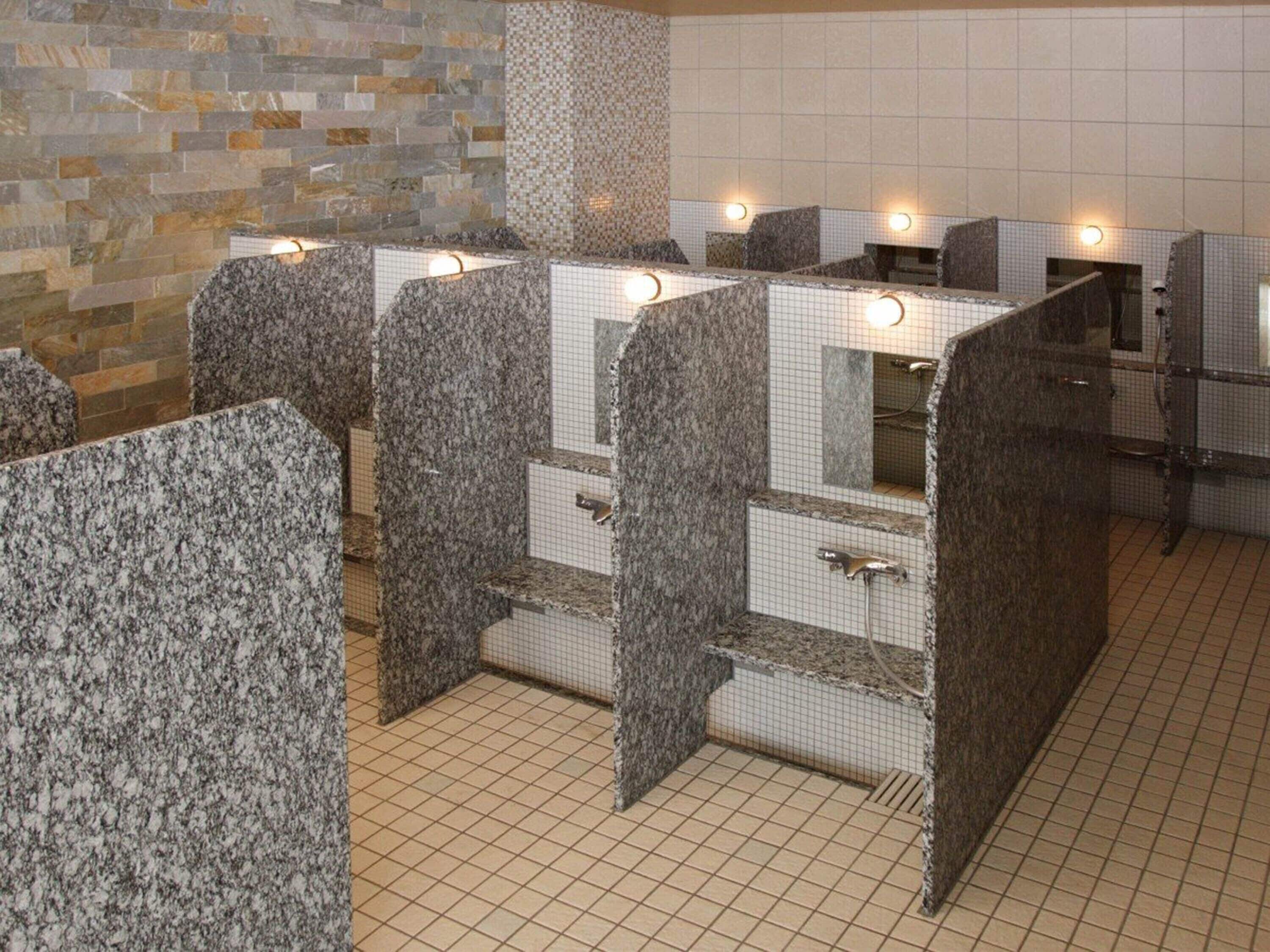 Des toilettes publiques dotées de comptoirs en granit, de murs carrelés et d’un sol carrelé.