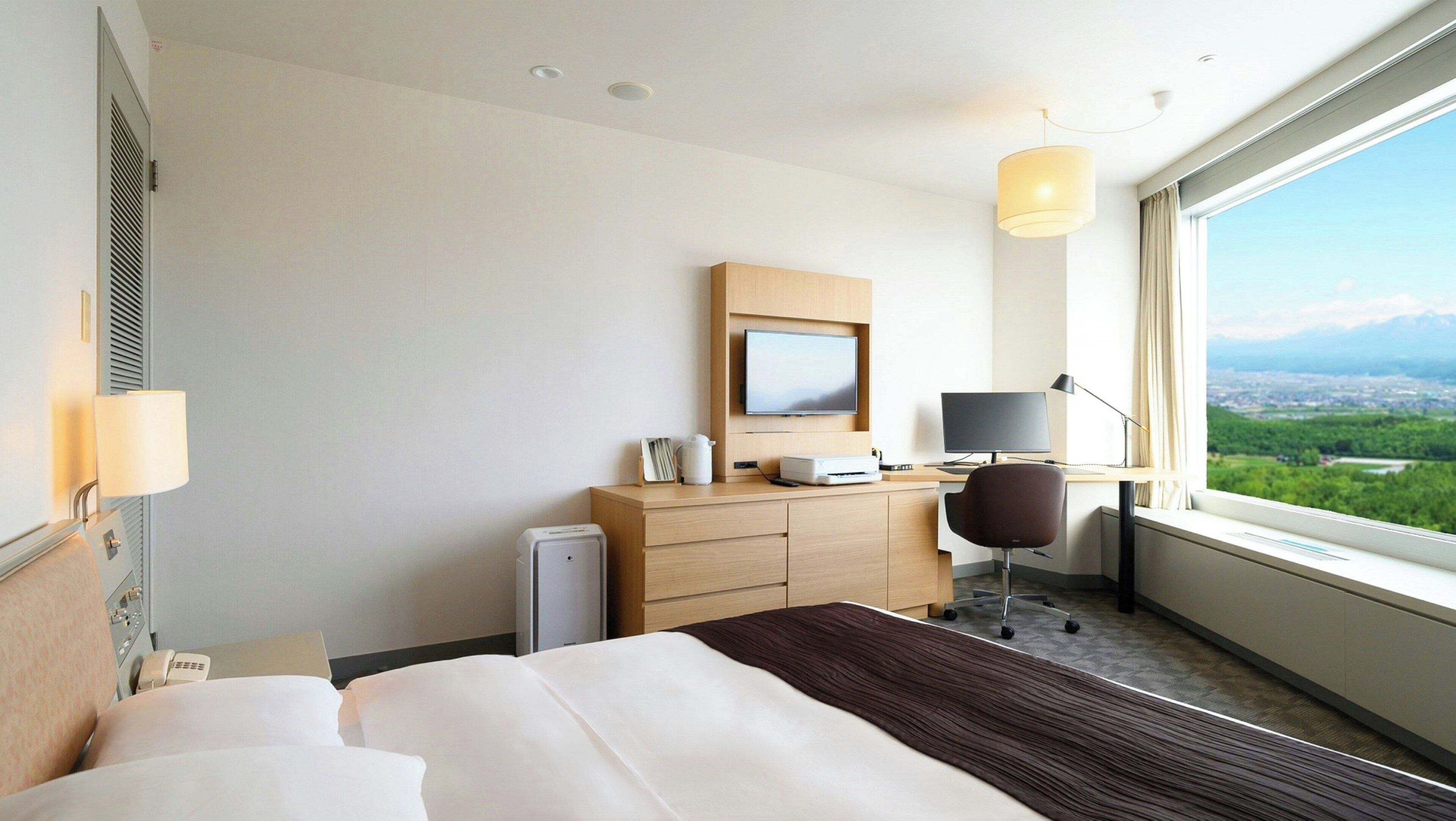 Una habitación de hotel con cama, escritorio, silla y un ventanal con vistas.