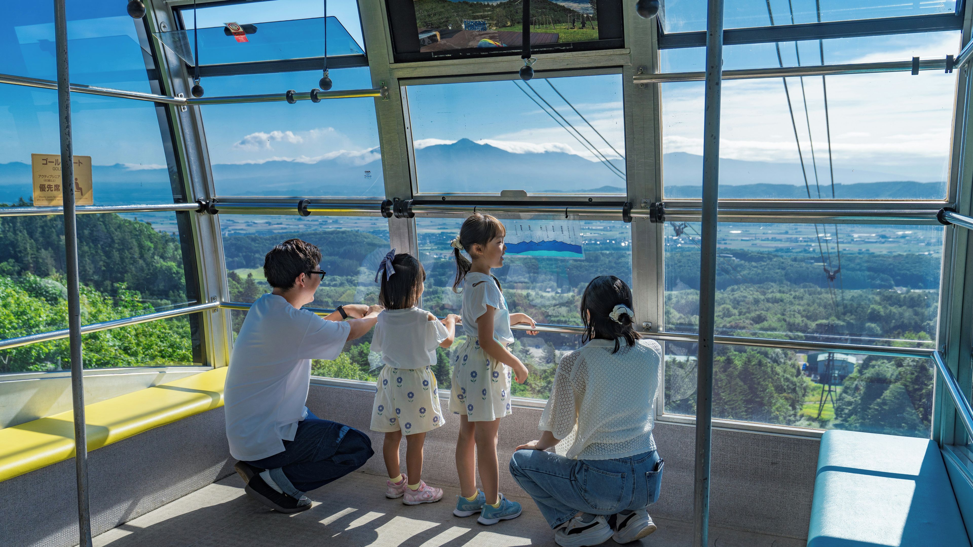 A group of people inside a glass-walled observation area, looking out at a landscape with mountains and greenery.
