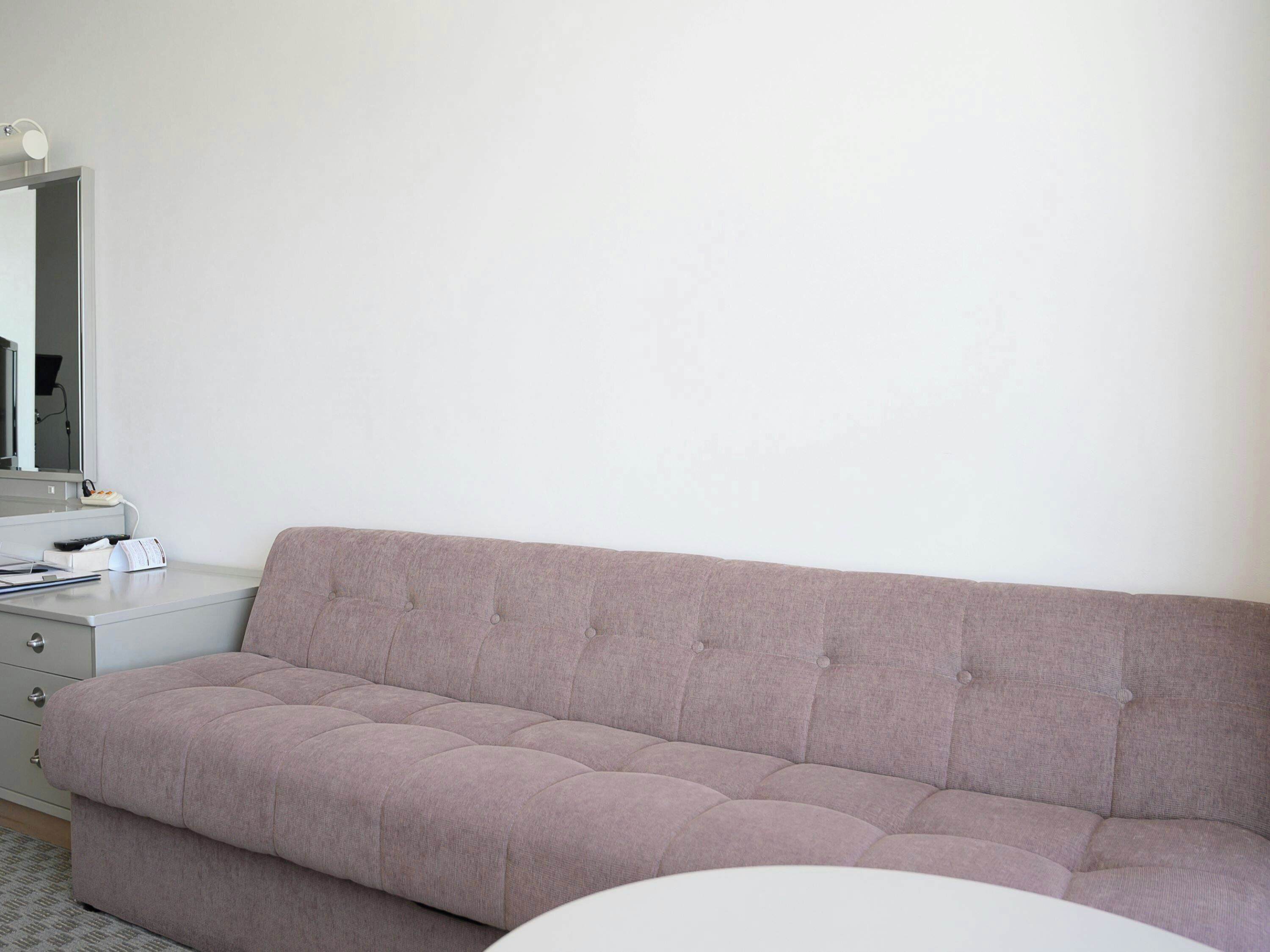 A neutral-toned room with a sofa, a small bedside table, and a mirror.