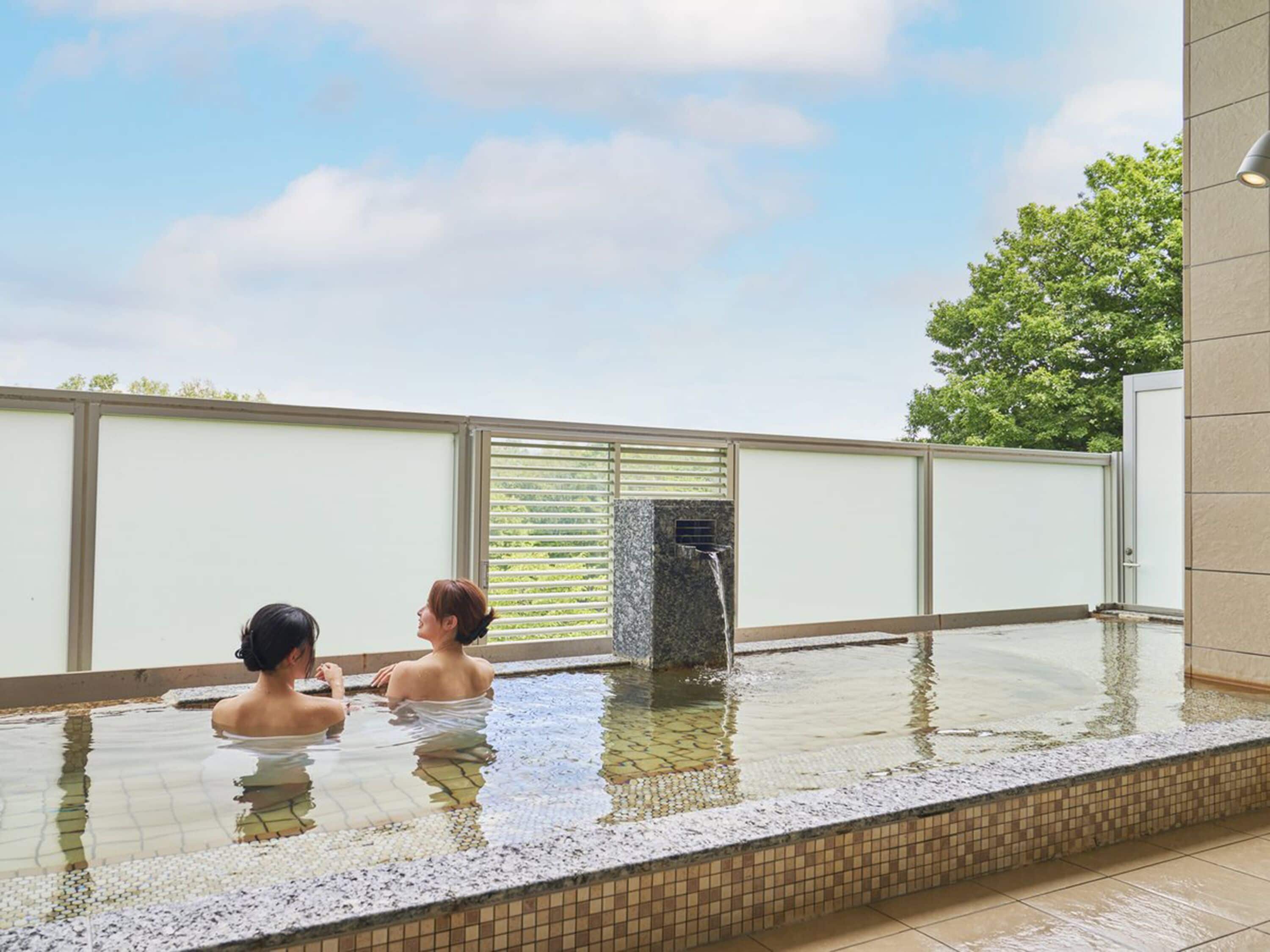 Una piscina con dos personas, rodeada por un patio de baldosas y una valla.