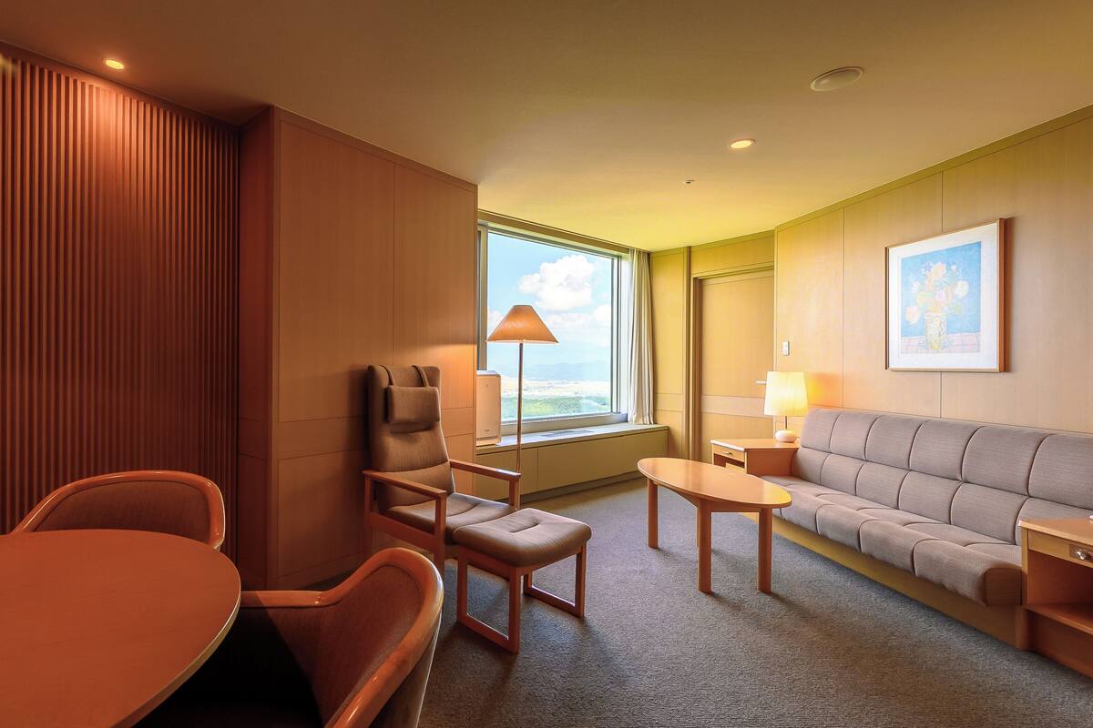 Quarto de hotel com parede de painel de madeira, um sofá, uma mesa, uma cadeira e um abajur.