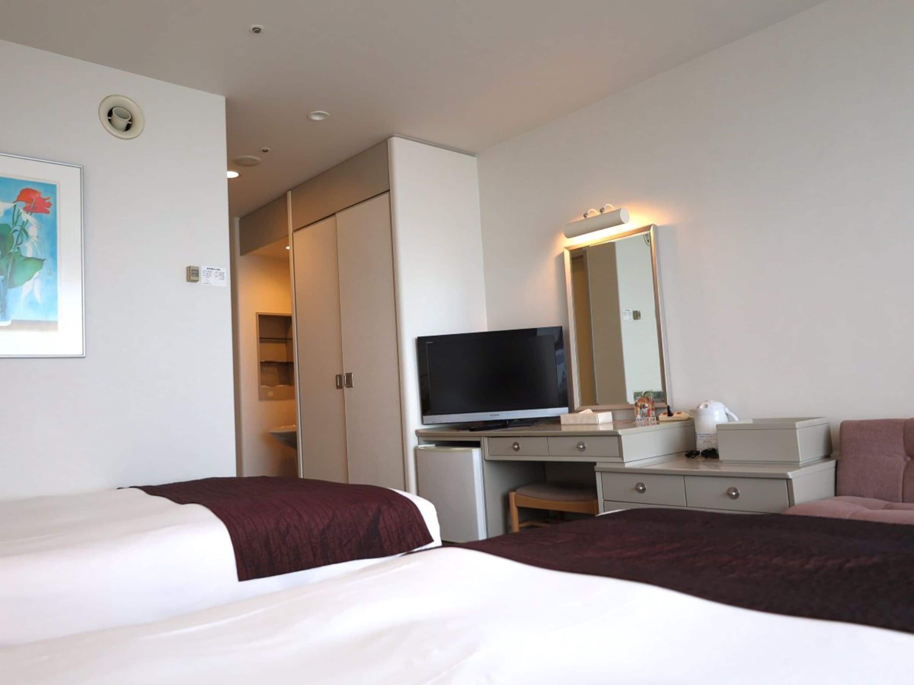 Habitación de hotel con dos camas, un escritorio con televisor, un espejo y un armario.