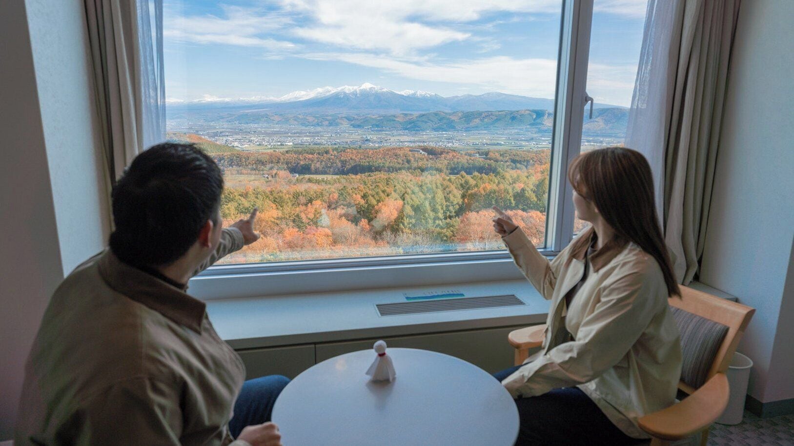 Two people seated at a table by a window with a view of a mountainous landscape.