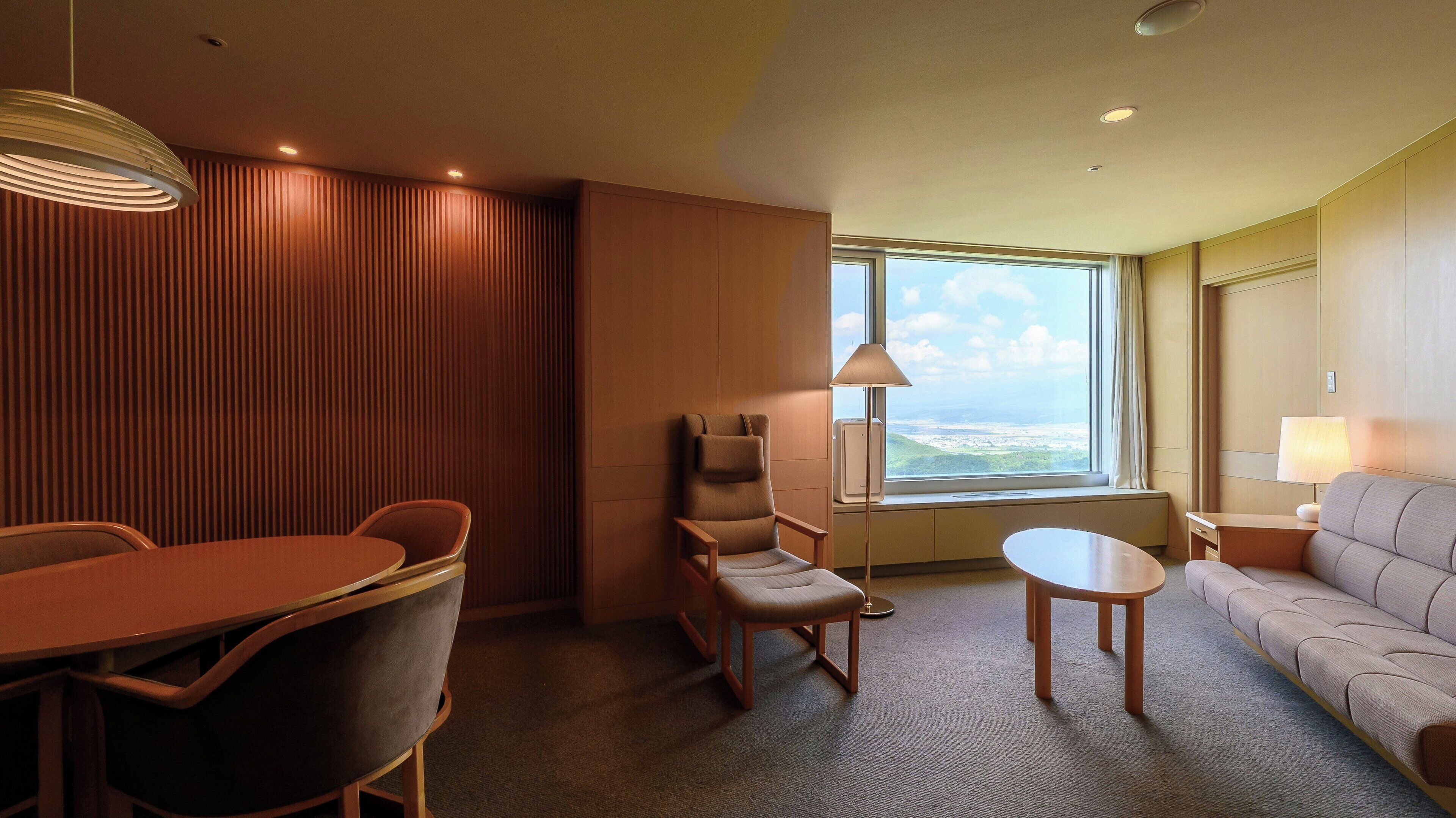 Ein Hotelzimmer mit Esstisch, zwei Stühlen, einer Couch, einem Fenster mit Blick und einer Lampe.