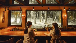 A bar with large windows offering a view of a snowy forest. - Shin Furano Prince Hotel (Furano)
