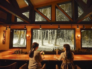 Um bar com janelas amplas que oferecem vista para uma floresta nevada.