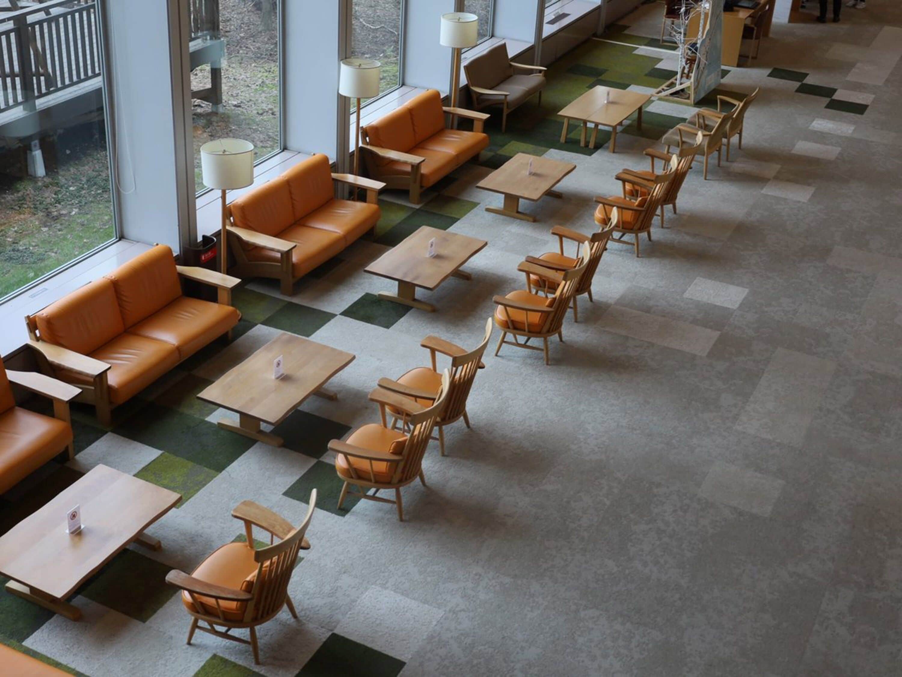 Een ruime binnenzitplaats met meerdere tafels en stoelen, grote ramen en een geruit vloerpatroon.