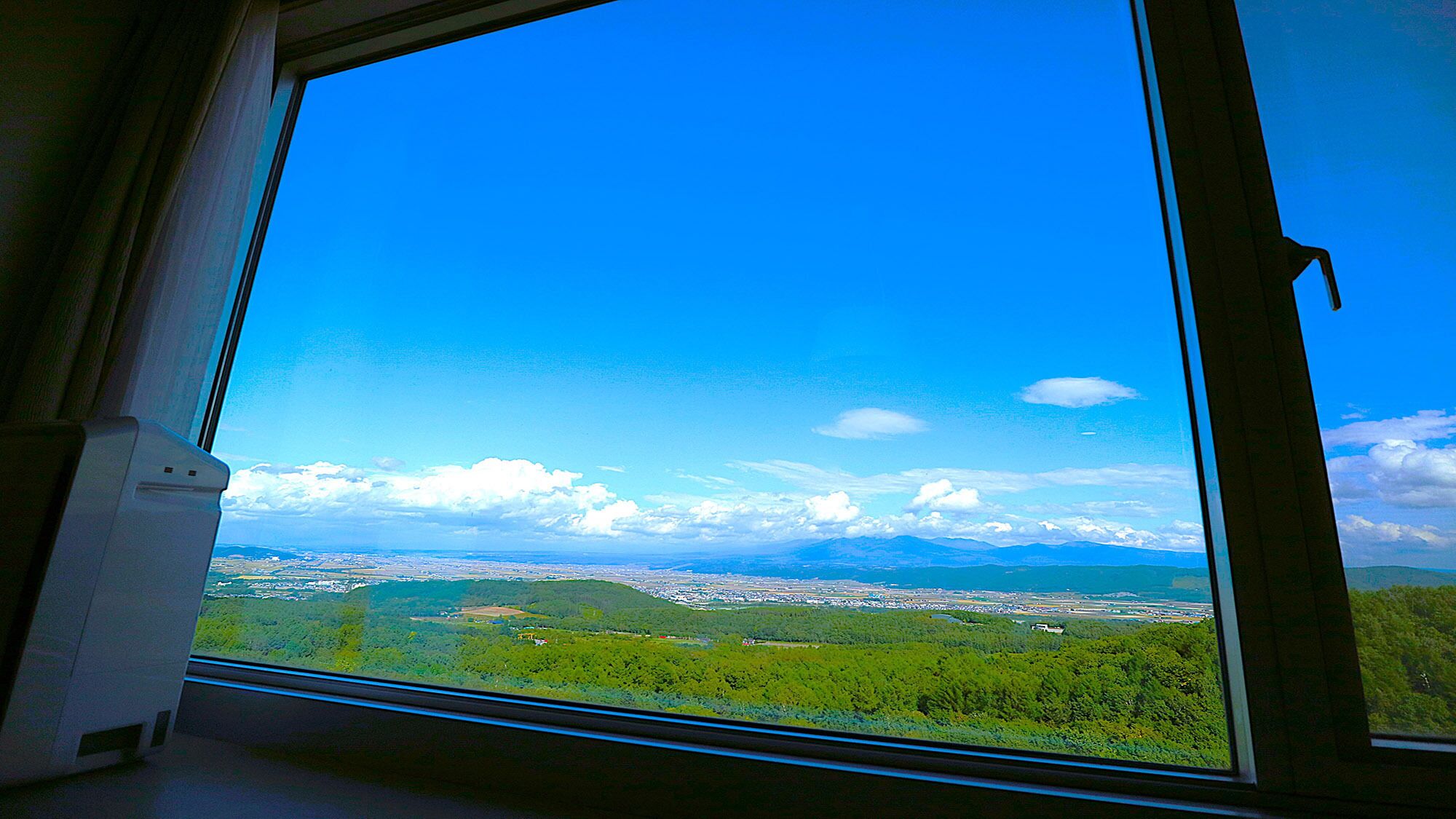 A window with a clear view of a landscape, including a body of water and distant mountains.