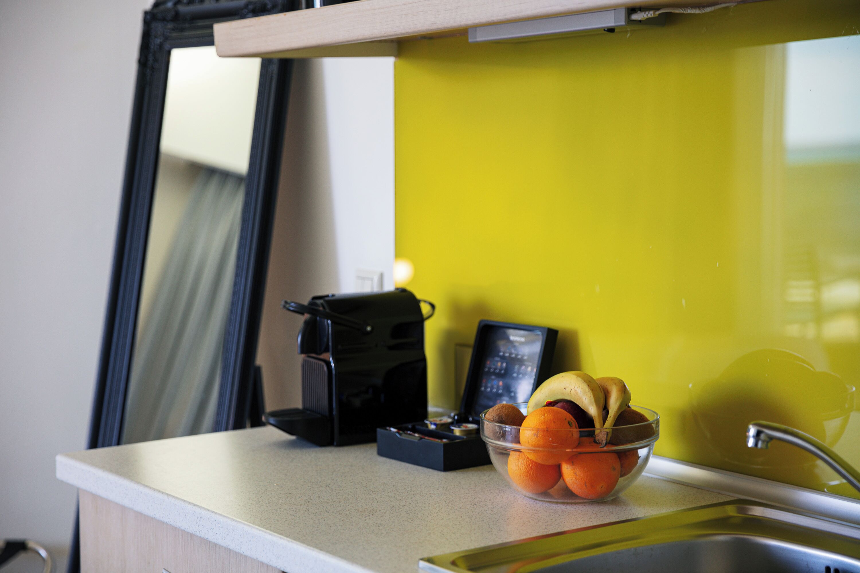 Una encimera de cocina con una cafetera, un cuenco de fruta y un fregadero.
