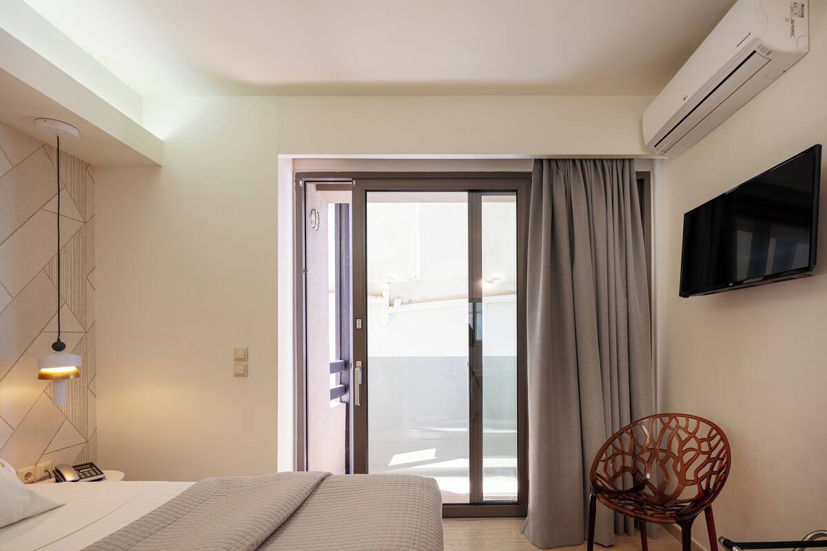 Une chambre d’hôtel équipée d’un lit, d’une chaise, d’une télévision, d’un climatiseur et d’une porte-fenêtre coulissante donnant sur le balcon.