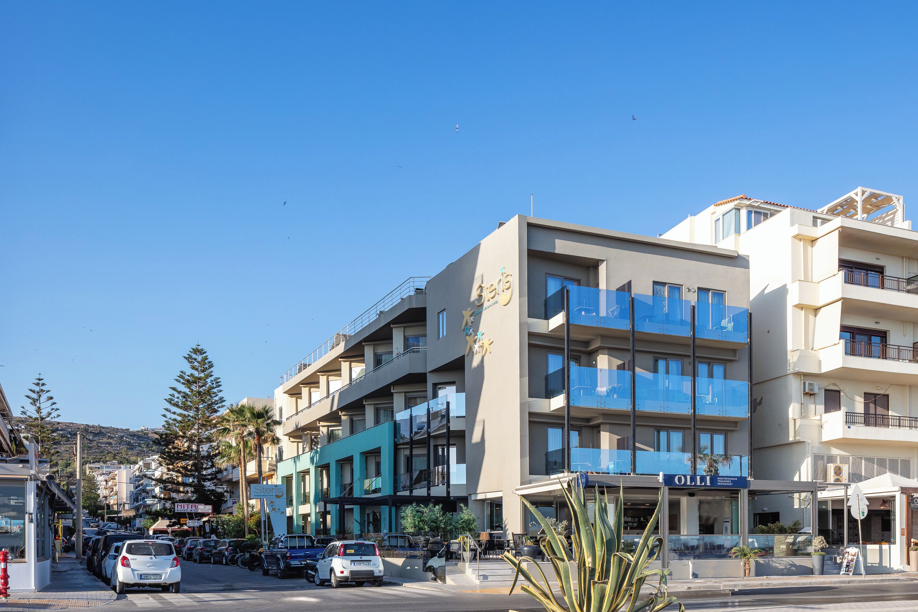 A multi-story hotel with balconies, a parking lot, and a clear sky.