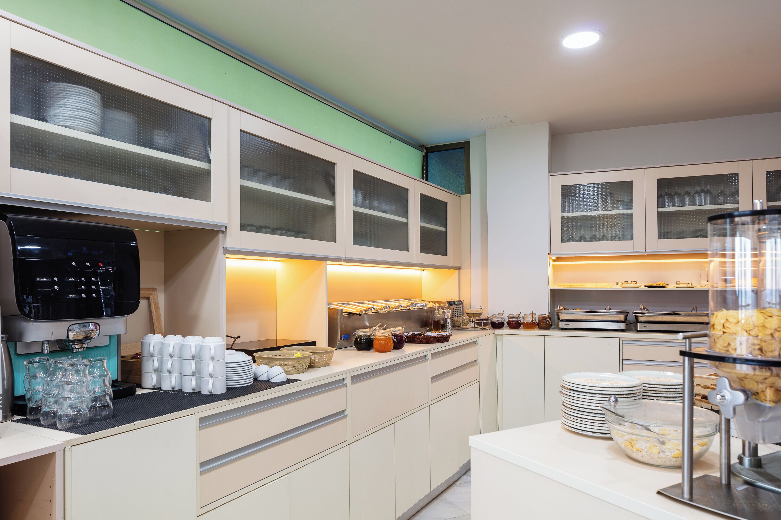 A modern kitchen with a coffee machine, glassware, and buffet-style food service.