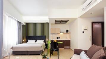 A hotel room with a bed, a desk, a sofa, a chair, and a small table with a plant and a remote control.