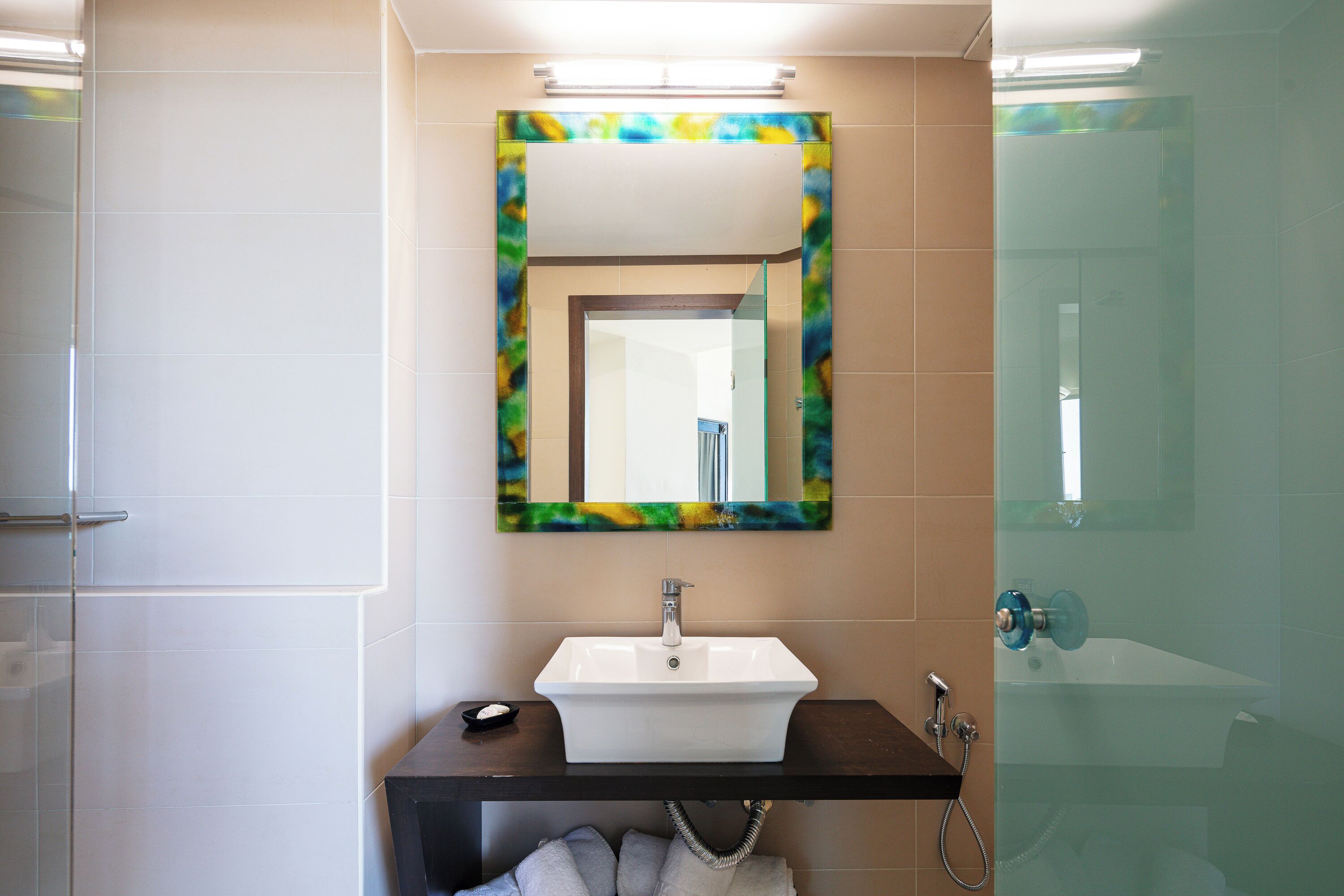 A bathroom with a white sink, a mirror with a colorful frame, and a glass shower enclosure.