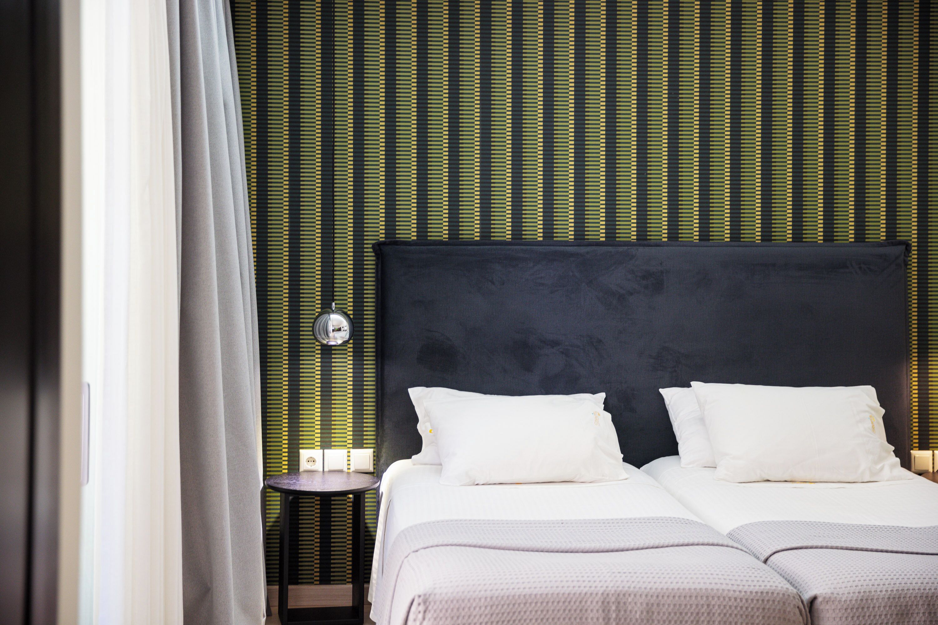 A hotel room with two beds, a dark headboard, and a striped wall pattern.