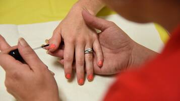 A close-up of hands with red nail polish, one hand holding a nail polish bottle.