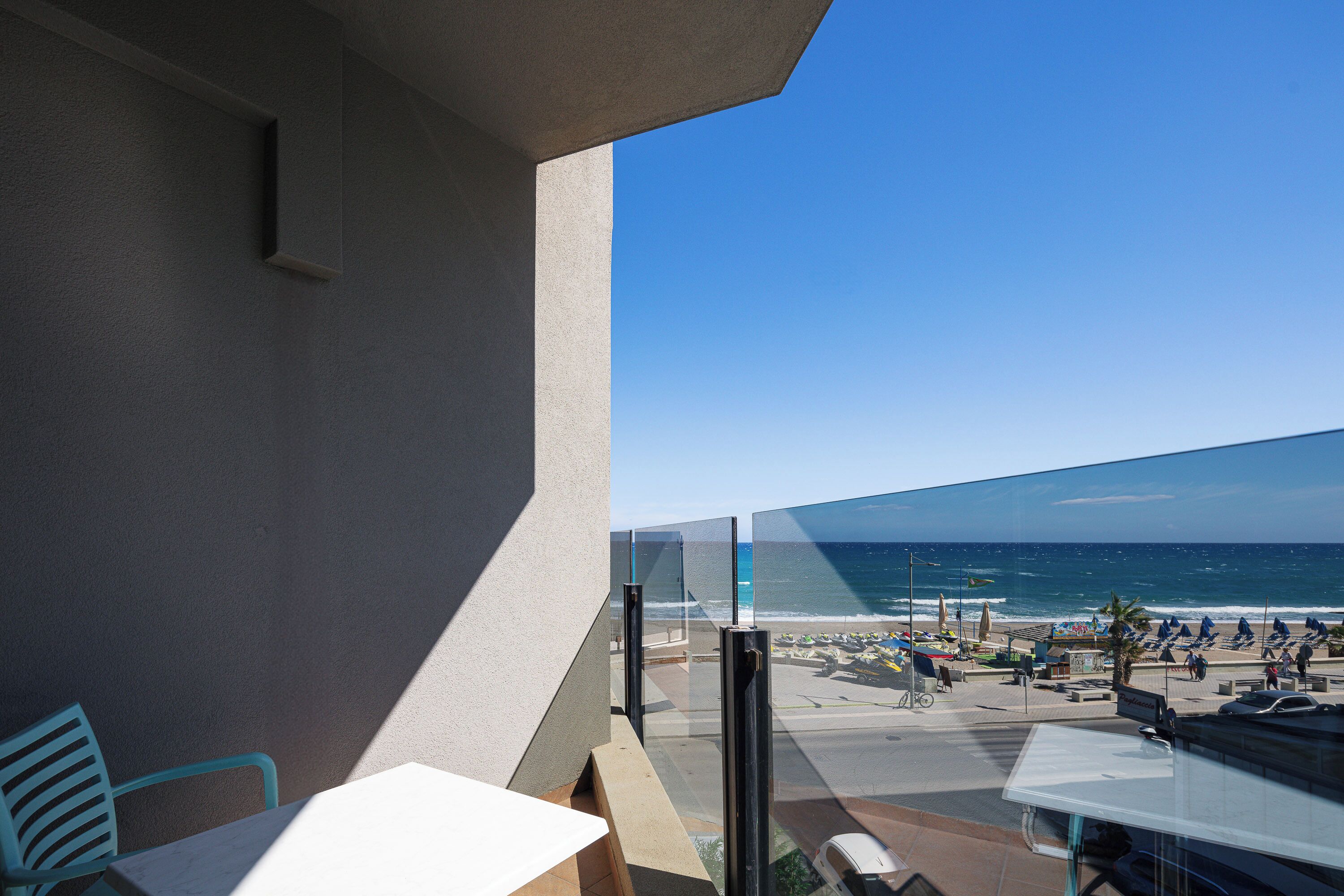Un balcón con vistas a la playa, mobiliario exterior y cielo despejado.