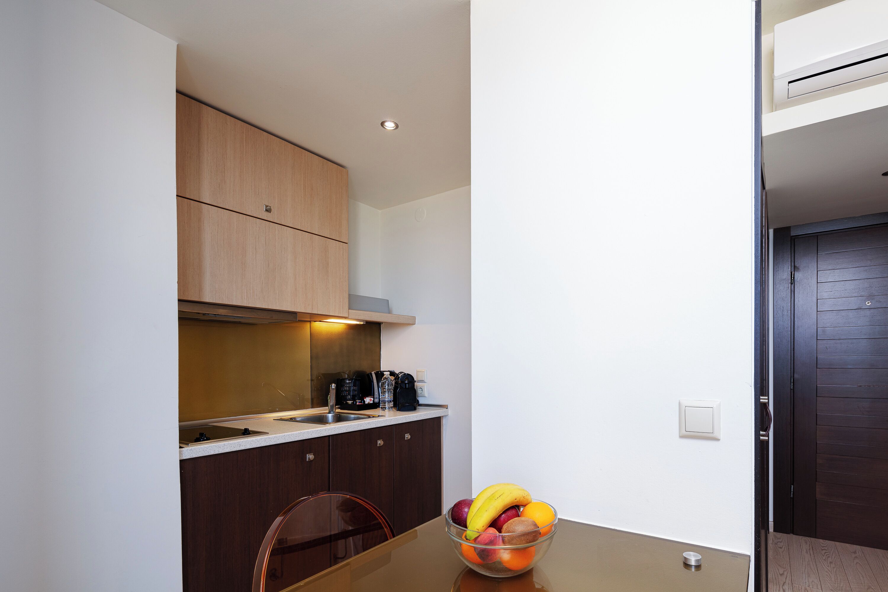 Una cocina moderna con armarios de madera, un lavamanos de acero inoxidable y un tazón de frutas sobre la mesa.