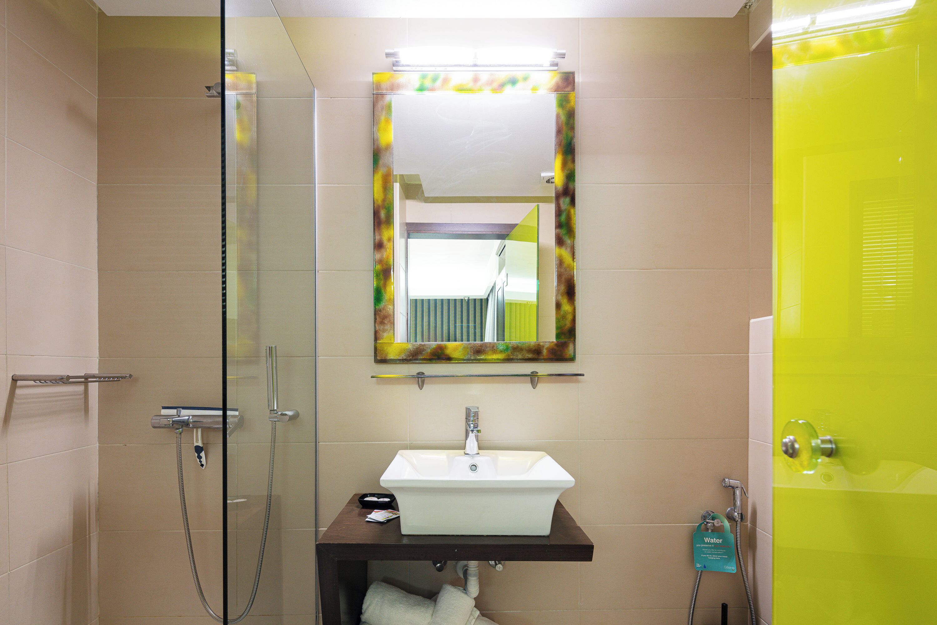 Un baño con cabina de ducha de vidrio, un lavamanos blanco con un espejo encima y una pared de acento amarillo brillante.