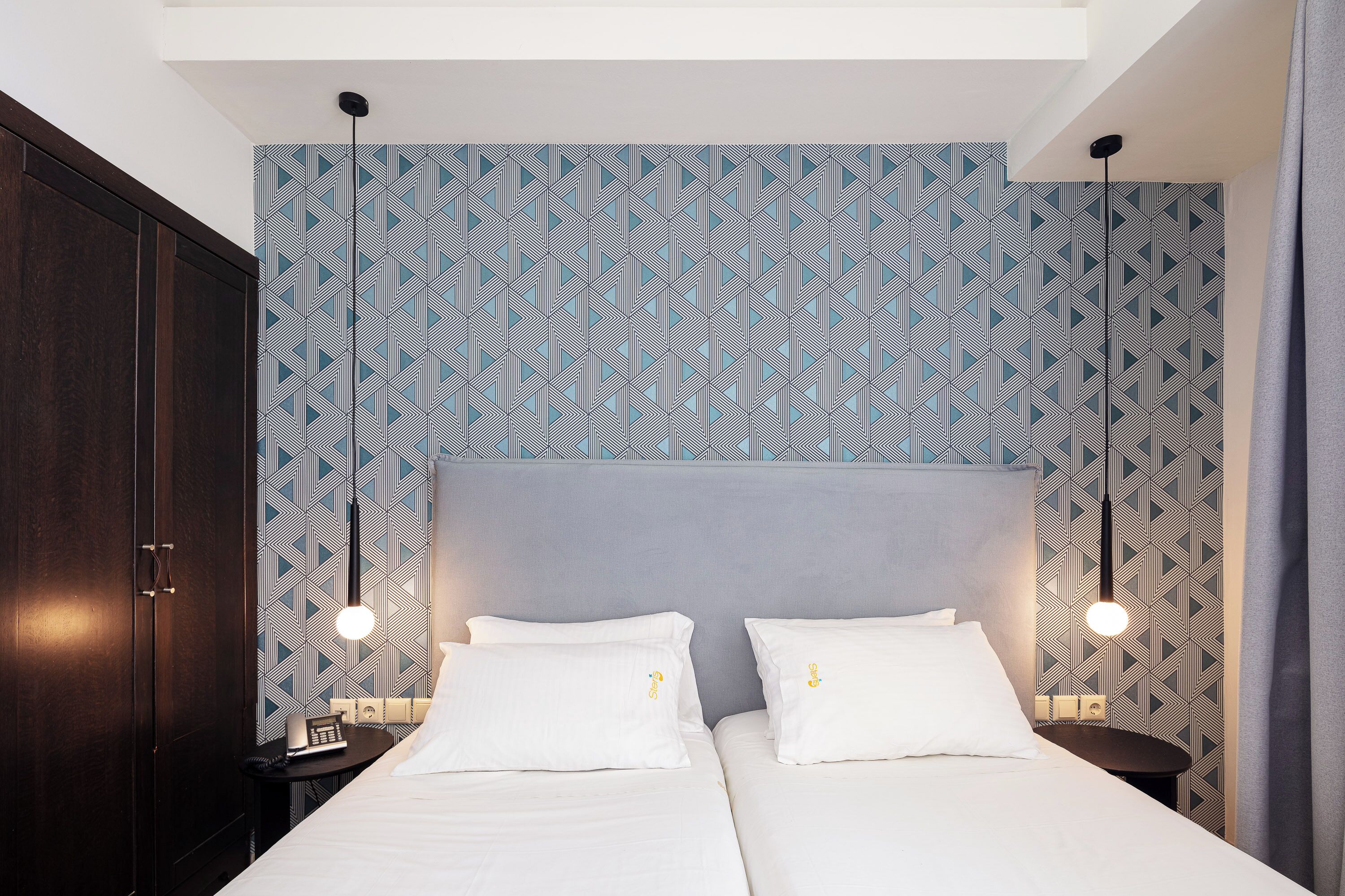 Una habitación de hotel con una cama grande, dos mesitas de noche y un papel tapiz estampado.