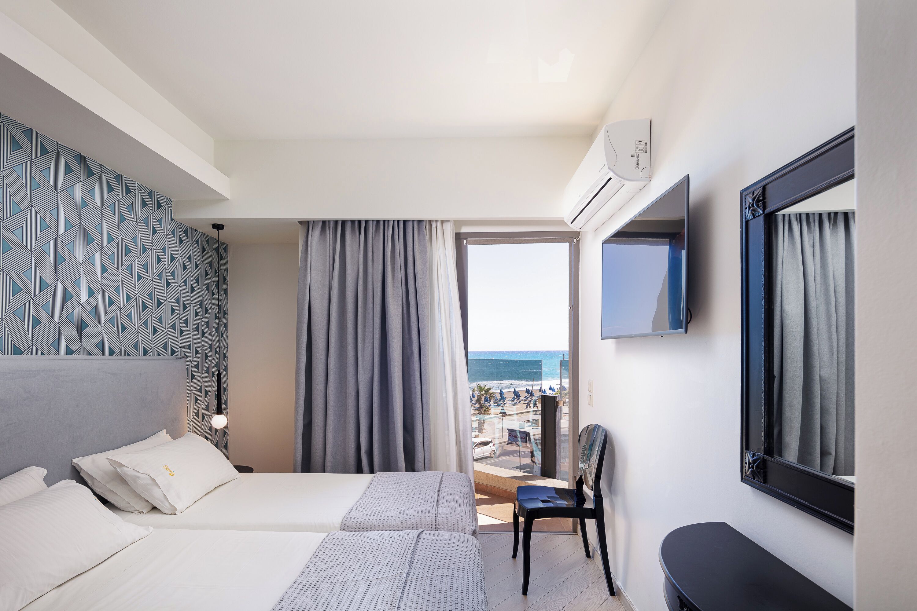 A hotel room with a bed, a chair, a TV, and a view of the beach.