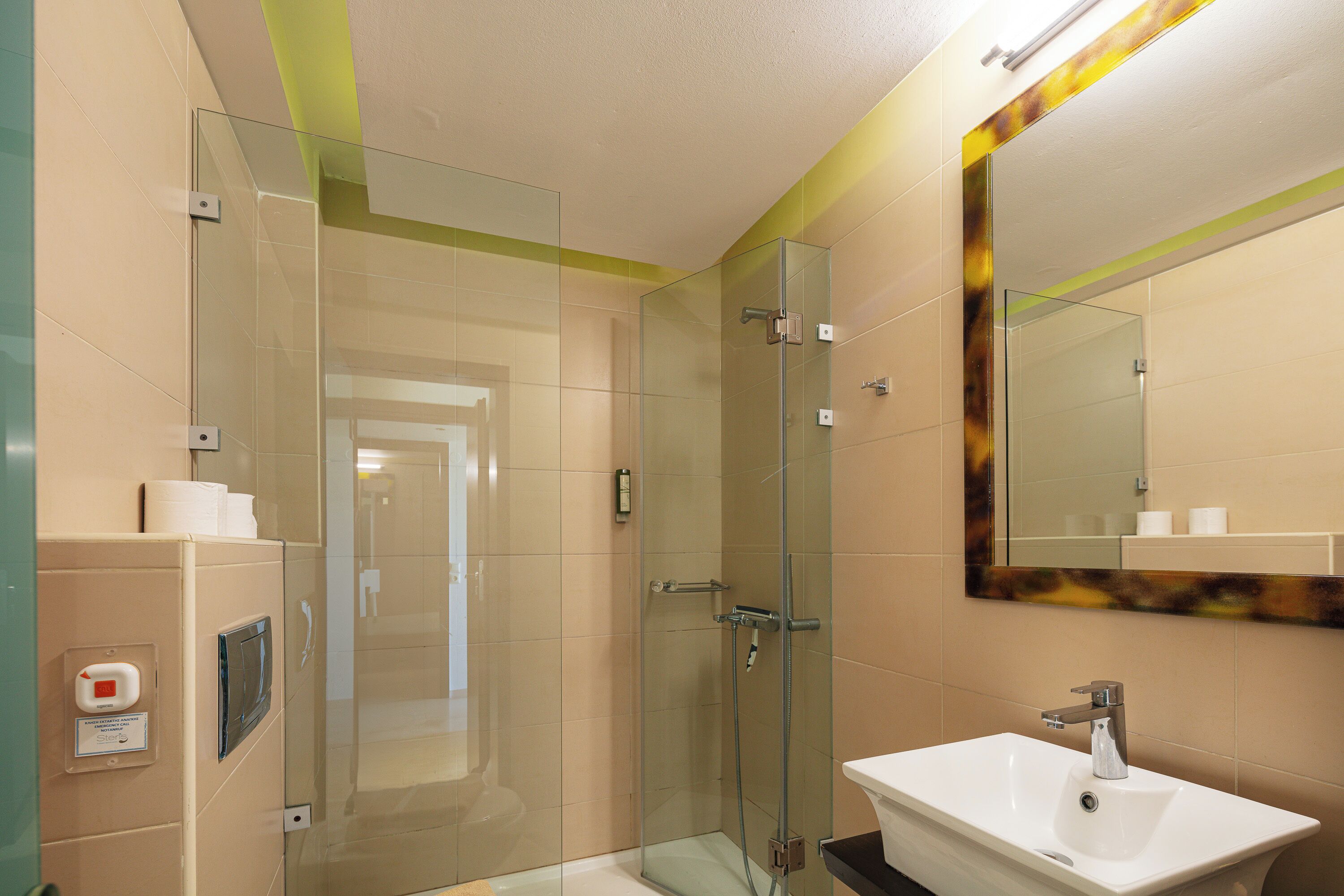 A modern bathroom with a glass shower enclosure, a white sink, and a mirror with a decorative frame.
