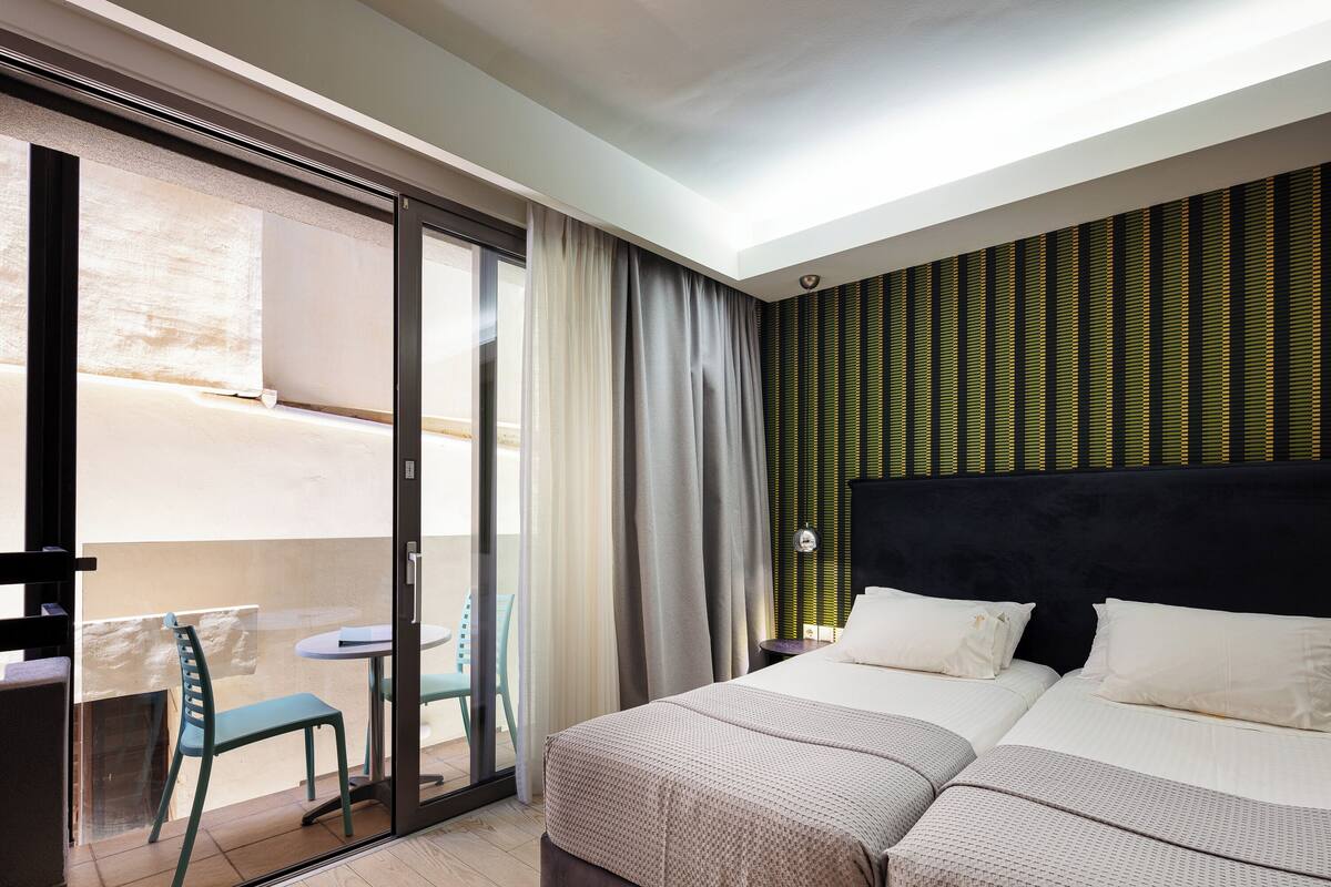 Une chambre d’hôtel avec un grand lit, une petite table, une chaise et une porte-fenêtre coulissante donnant sur un balcon.