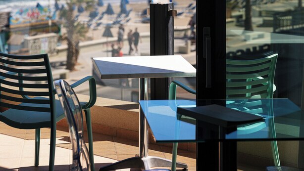 Een café aan het strand met terras, uitzicht op de oceaan en strandparasols.