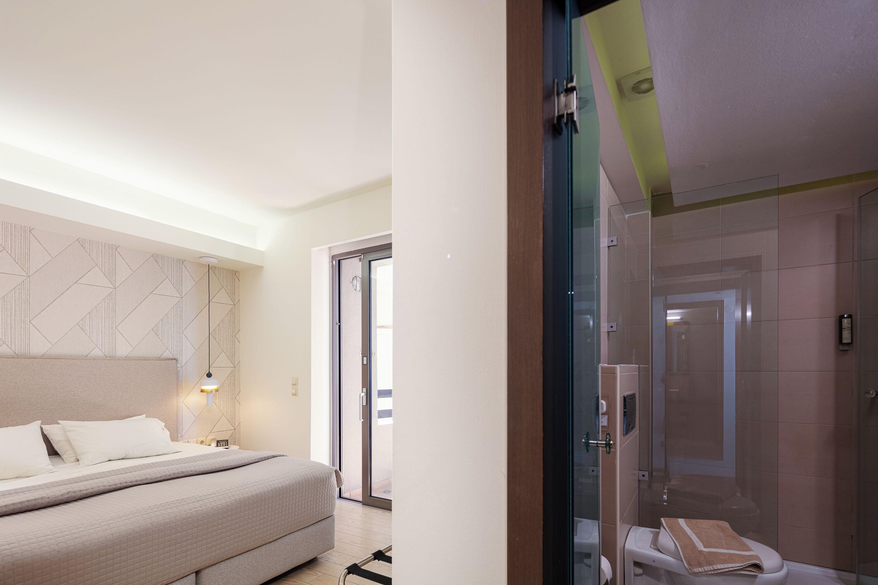 A modern hotel room with a large bed, a glass shower enclosure, and a view through the glass door.