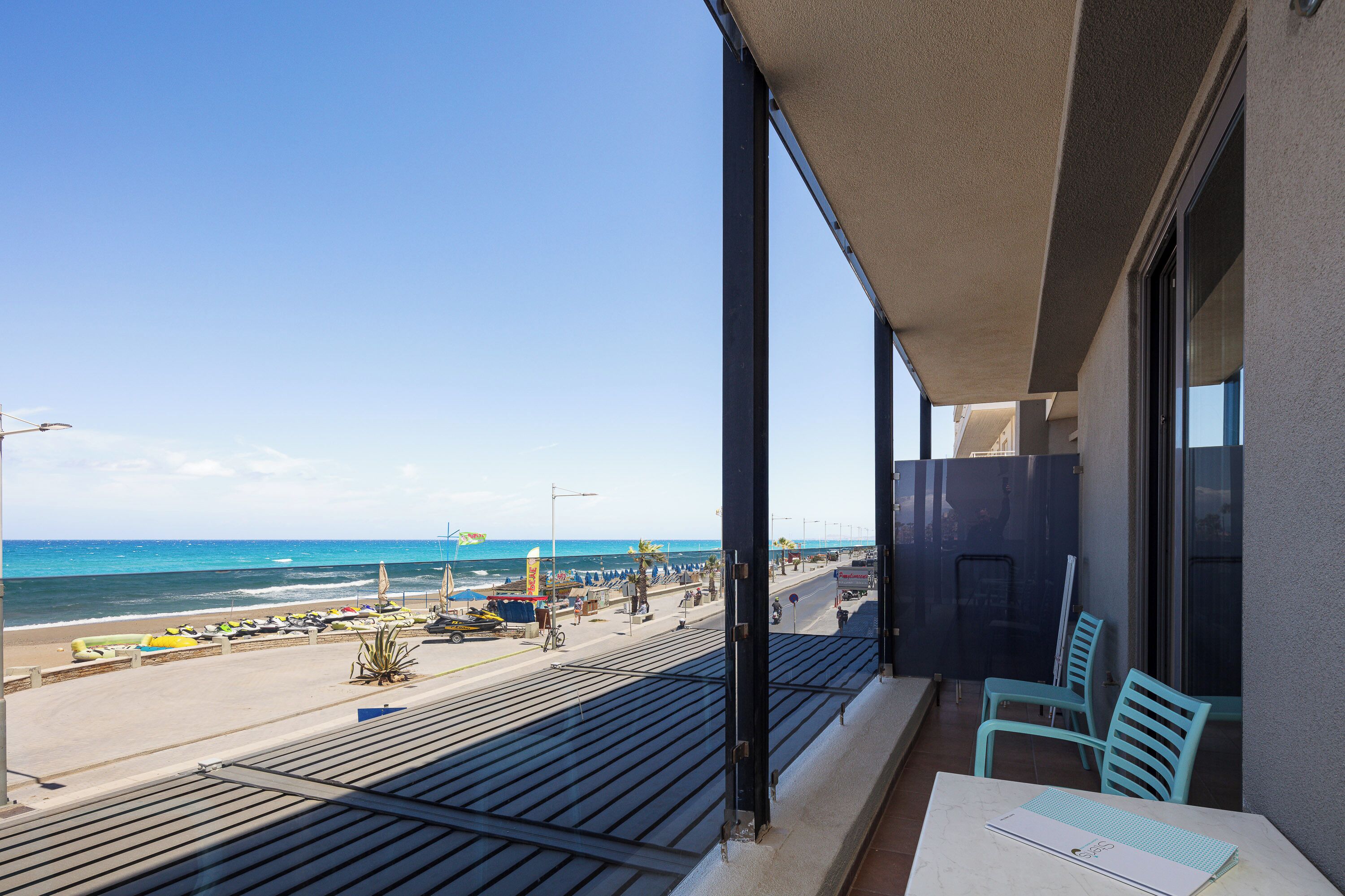 A balcony with a view of the beach, a table with a chair, and a window with a view of the ocean.