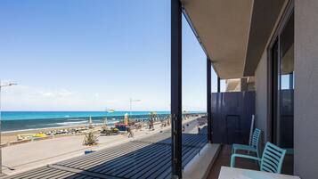 A balcony with a view of the beach, a table with a chair, and a window with a view of the ocean.