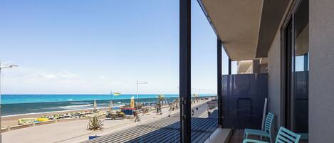 A balcony with a view of the beach, a table with a chair, and a window with a view of the ocean.