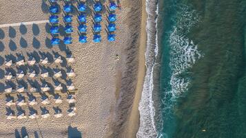 An aerial view of a beach with rows of blue umbrellas and several boats lined up along the shore.