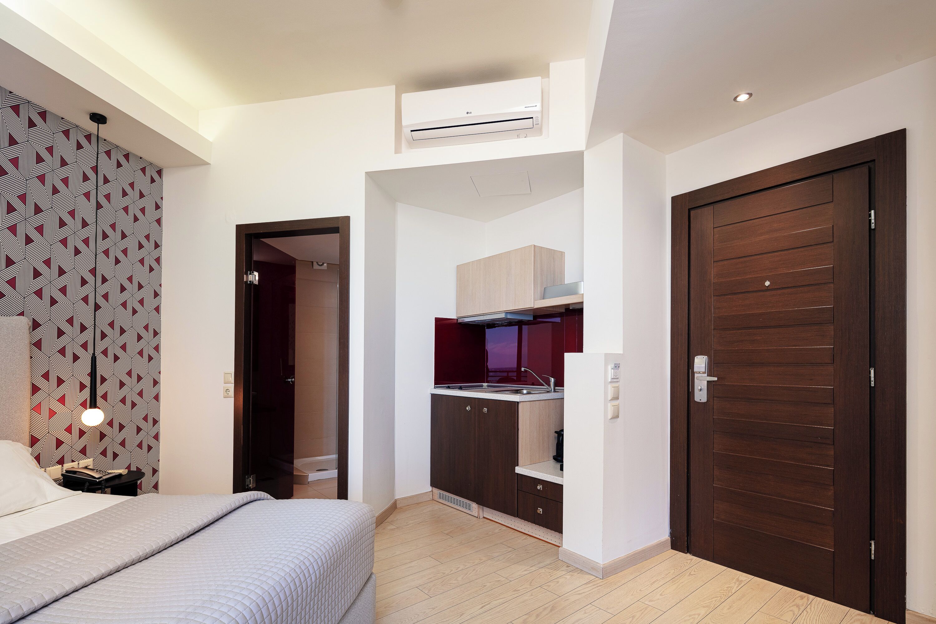 A compact bedroom with a bed, a bedside table, a wardrobe, and a built-in kitchenette with a stove and sink.