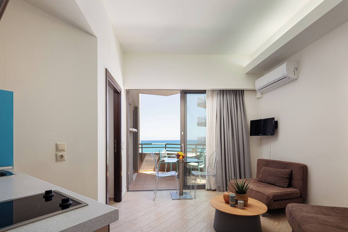 Un salon moderne avec un balcon, un téléviseur à écran plat, un canapé et une petite table agrémentée d’une plante.